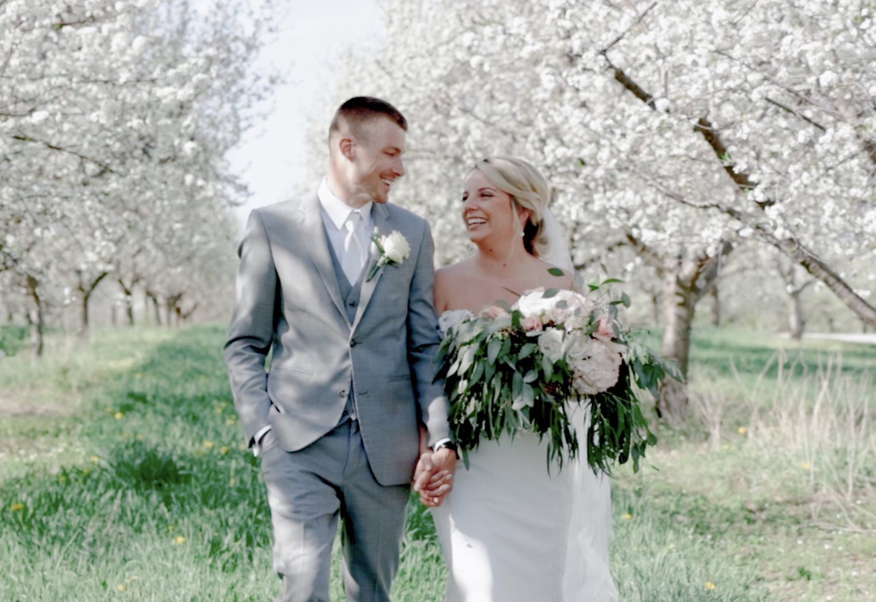 Bride and groom walking through cherry orchards during Traverse City Cherry Blossom wedding at Bay View Weddings