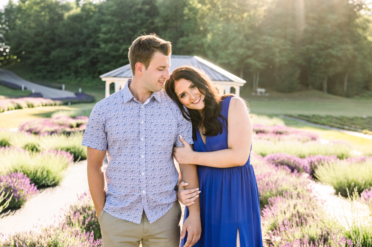 Lindsey resting her head on Austin's shoulder while she holds his arm and he looks down at her during their engagement session at a lavender farm