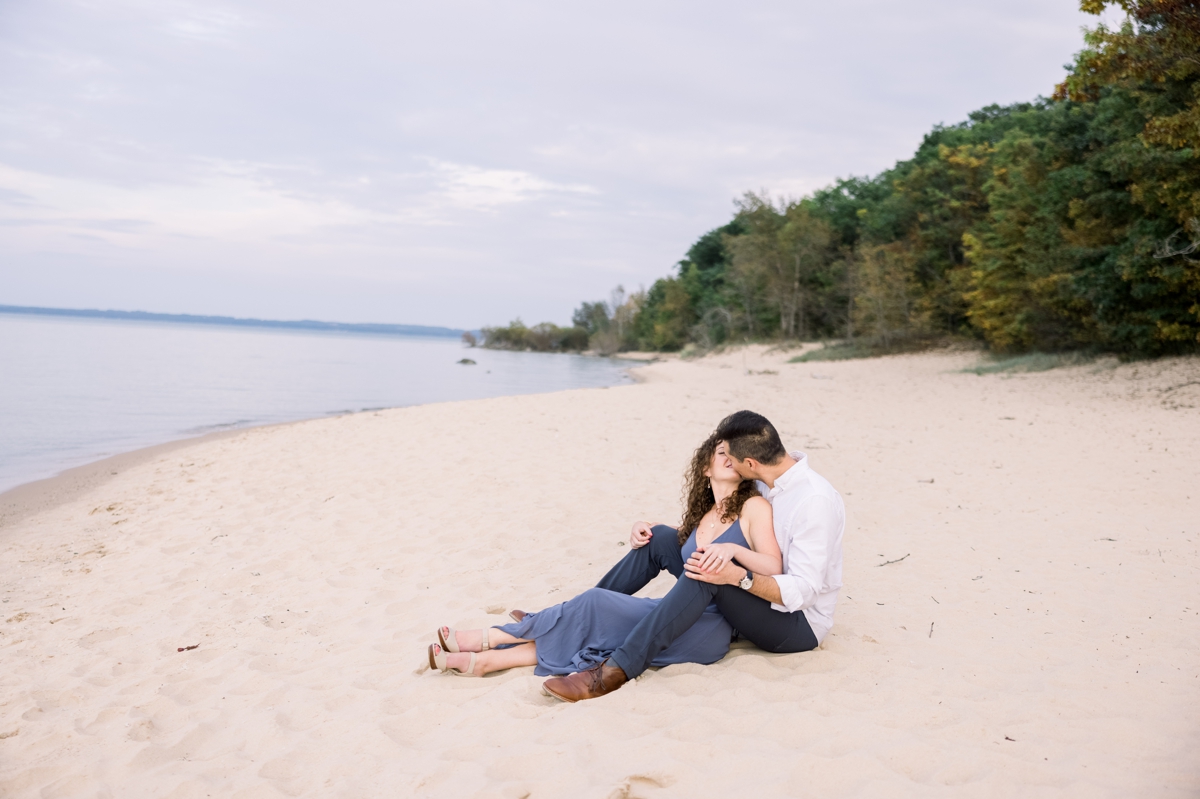 Marissa and Alex snuggling in the sand during their beach engagement session.