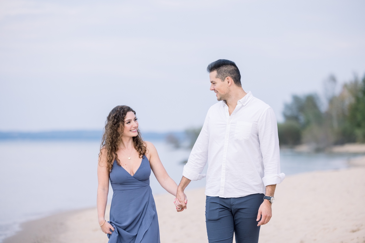 Marissa and Alex walking hand in hand along the beach during their engagement session.