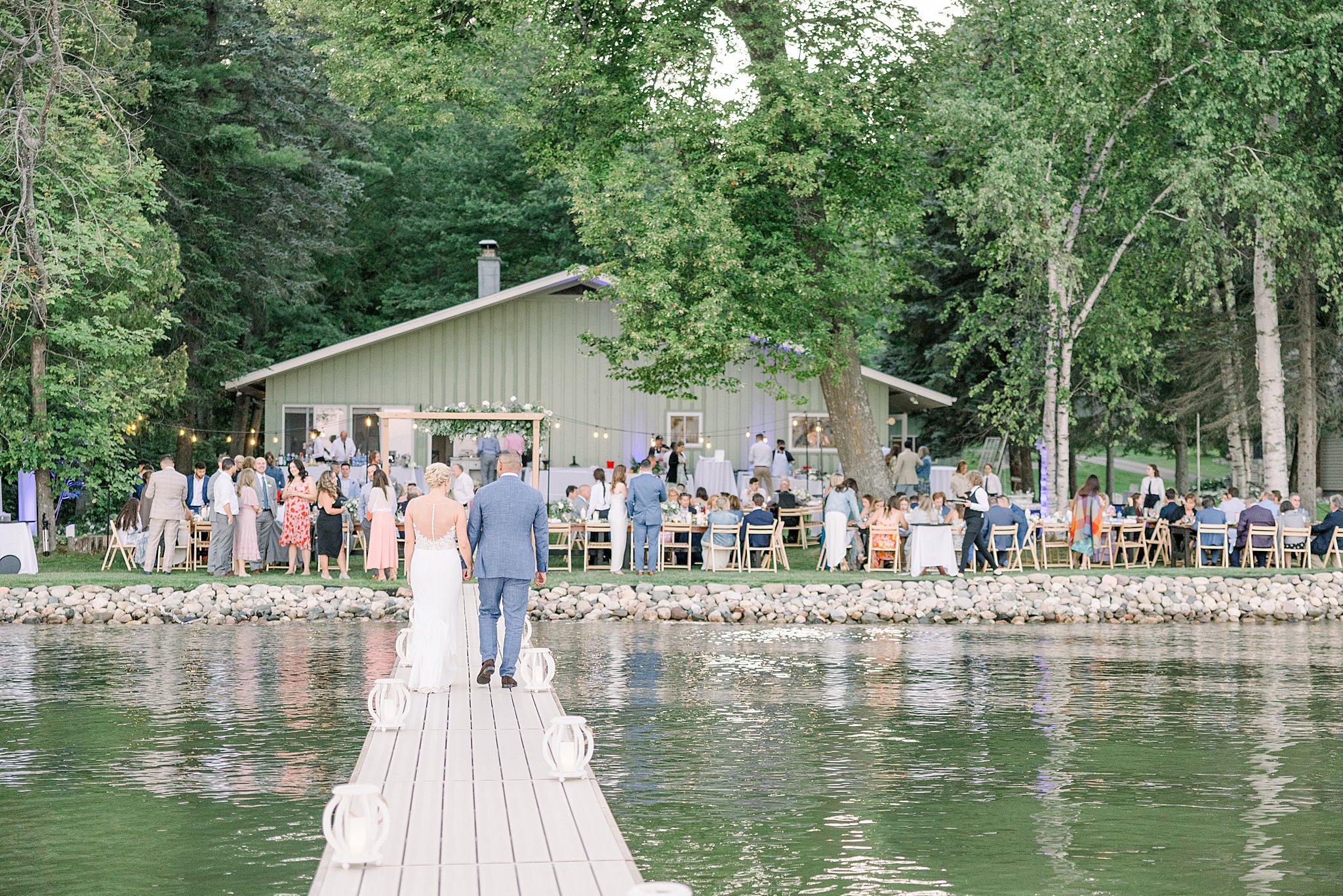 Bride and groom walk down dock to return to their wedding reception after enjoying some time together during their lakeside wedding on the shores of Burt Lake in Northern MIchigan.